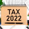 Text TAX 2022 on note pad, calculator, chart, magnifier. Accounting concept. Flat lay.
